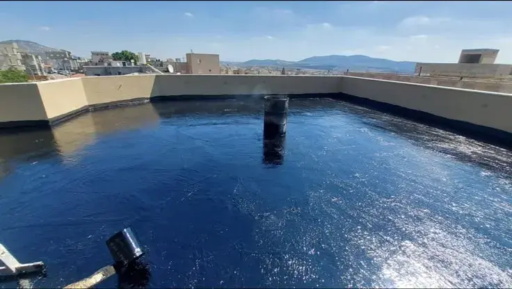 גג שטוח מוקף מעקה, מצופה בשכבת איטום שחורה ומבריקה סביב פתחי הניקוז
